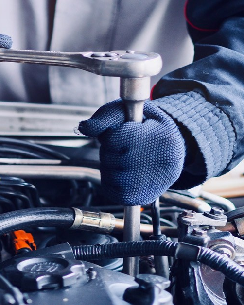 Mechanic in blue gloves using a wrench to work on a car engine, close-up.