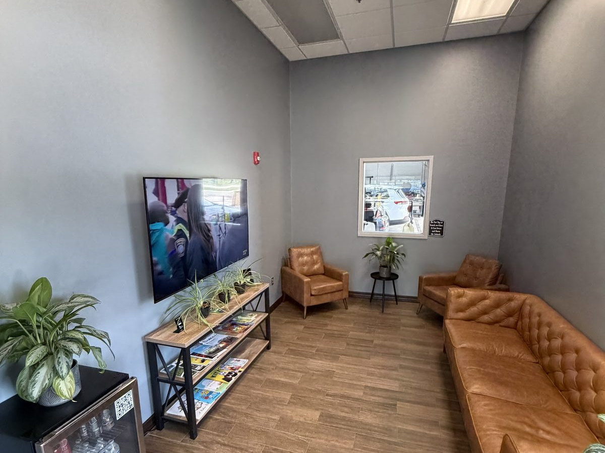 The customer waiting area at First Call Auto Care in Royal Oak, MI, with leather seating, a television and a drinks cooler