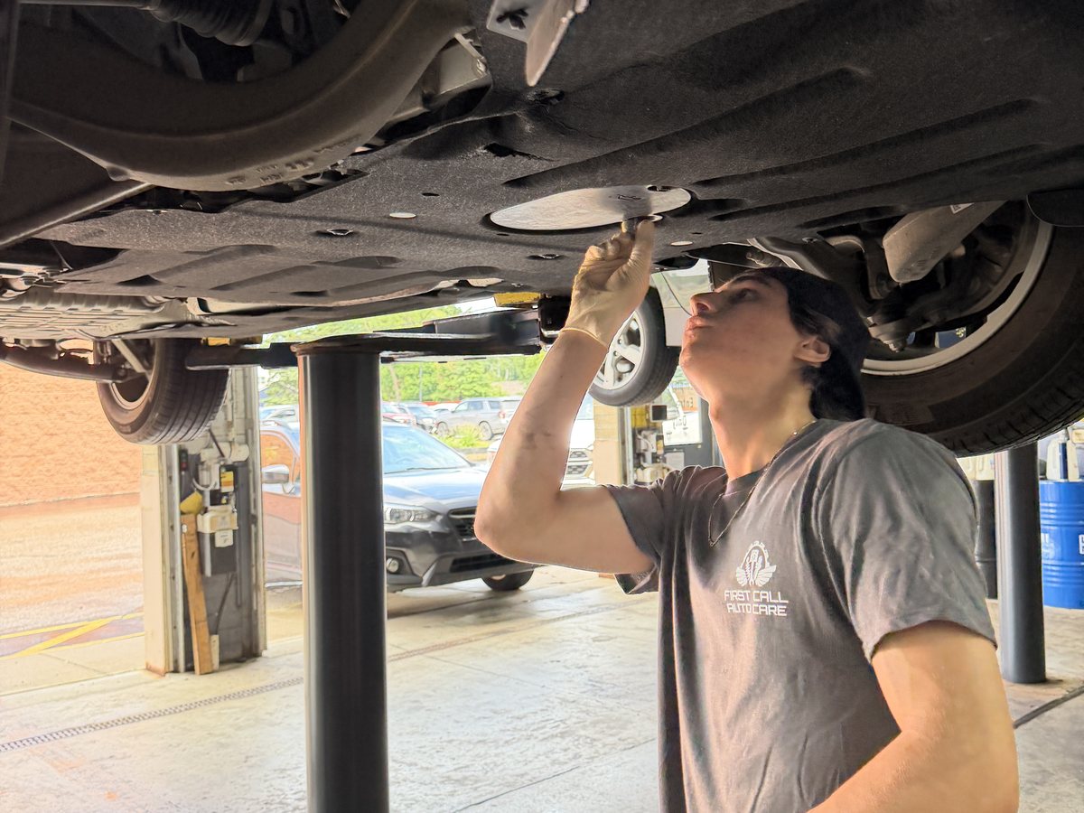 A First Call Auto Care technician inspecting the underside of a used vehicle raised on a lift in Royal Oak
