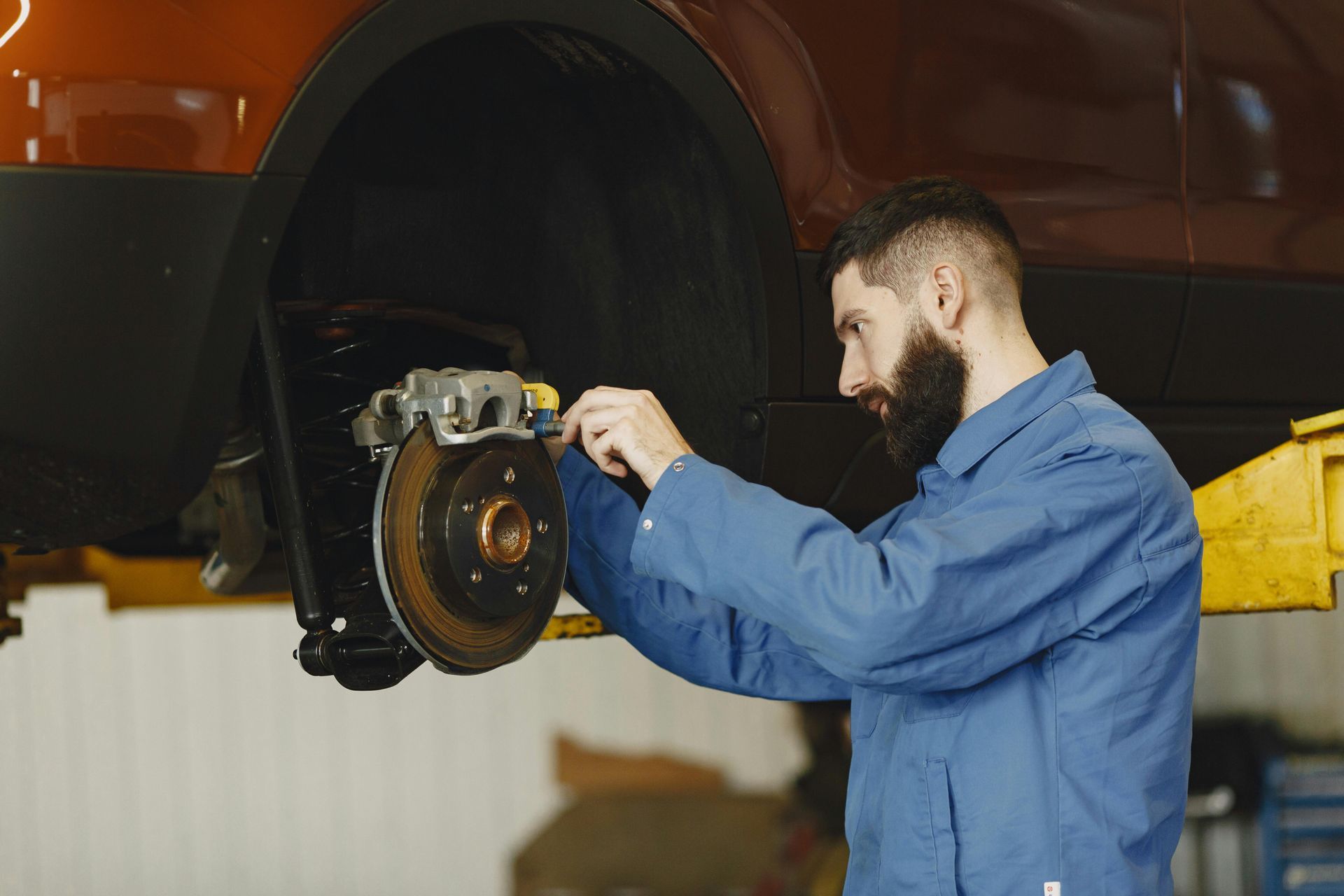 Mechanic in blue coveralls working on a car's brake system in a repair shop.